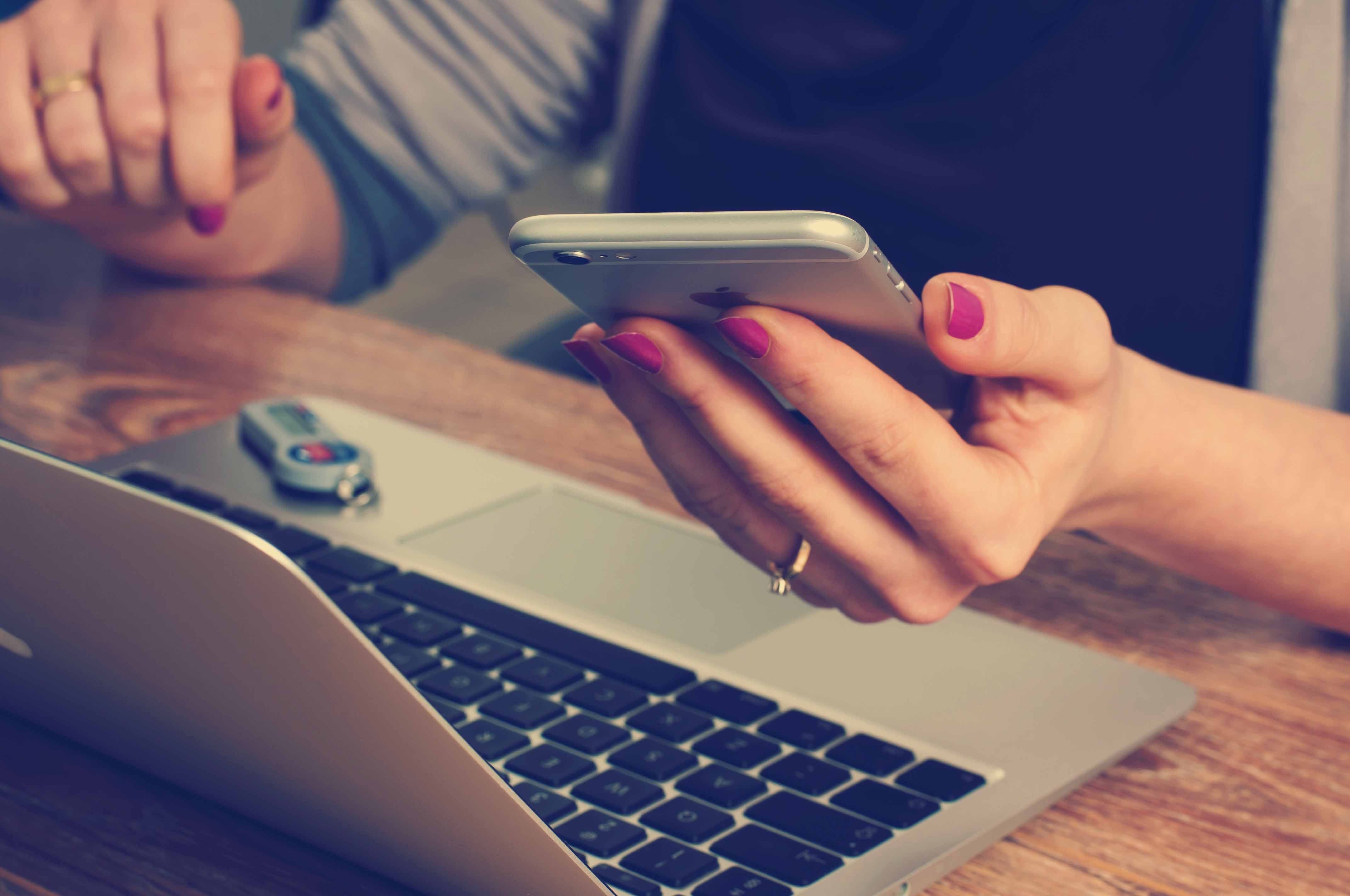 Laptop on a table with a woman's hand hold a cellphone